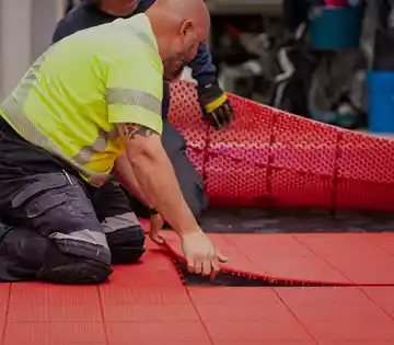 Installer securing red modular court tile flooring for a commercial sport court