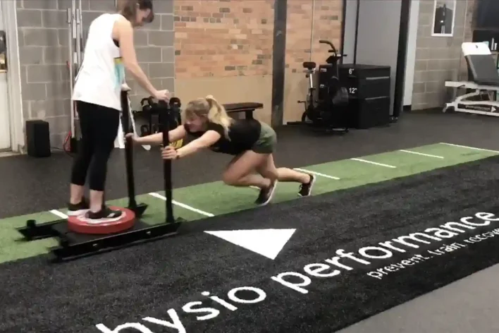image of woman pushing athletic sled on synthetic turf